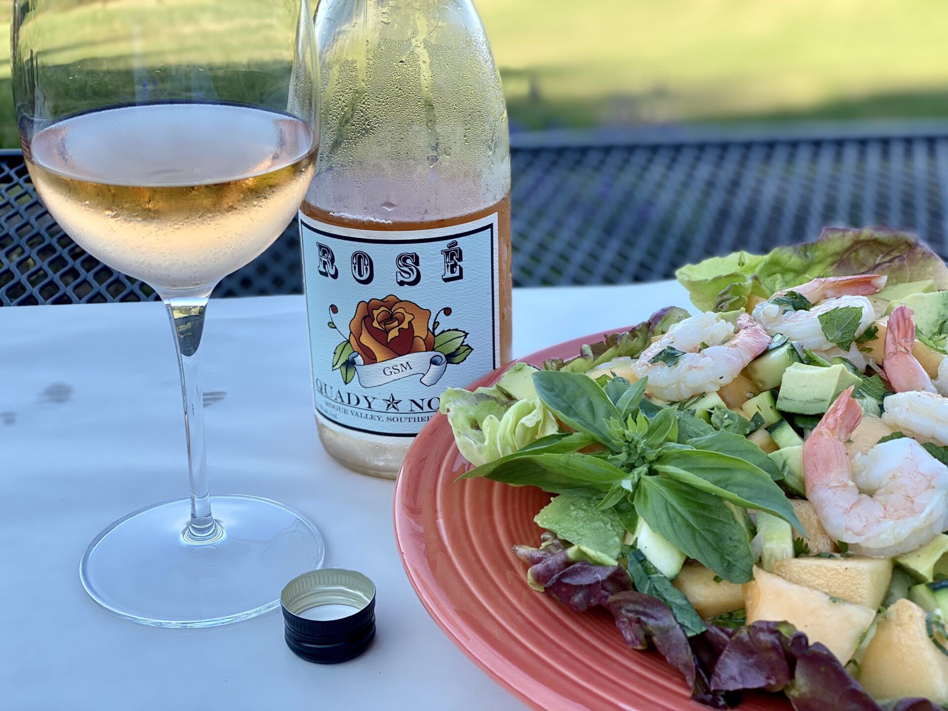 a bottle and glass of rose wine with shrimp melon salad
