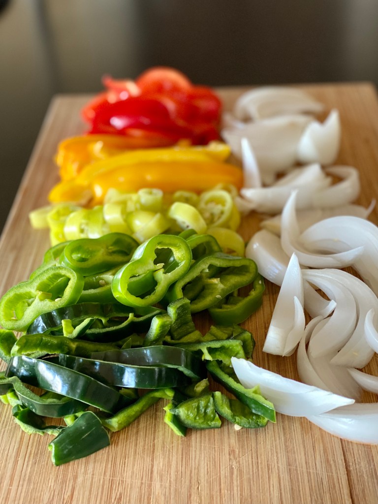 A rainbow of sliced peppers and white onion on a cutting board.