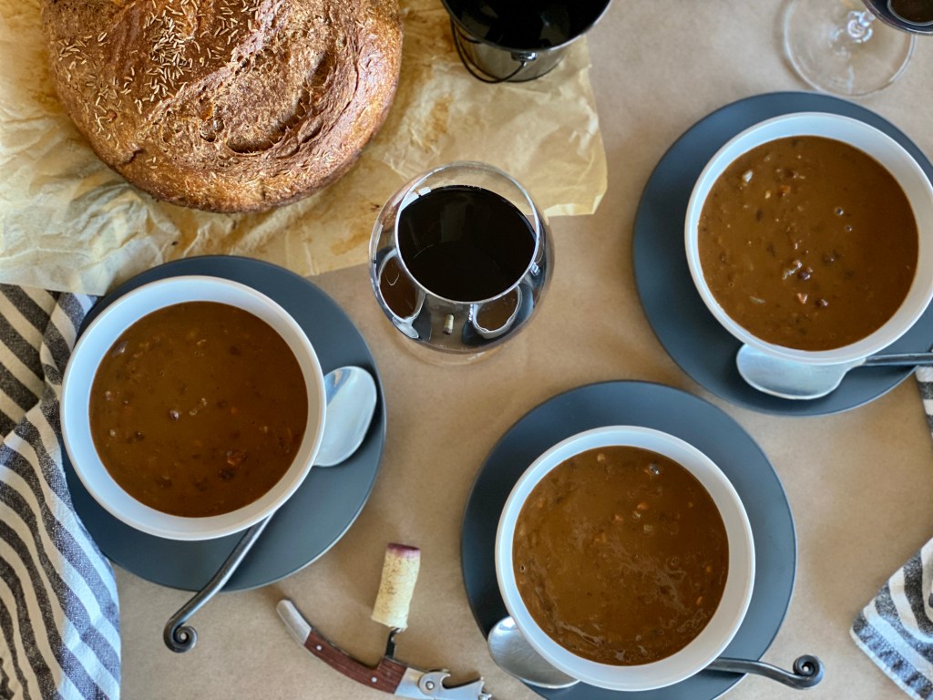 Overhead photo of bowls of pumpkin black bean soup, bread loaf, and wine glasses.