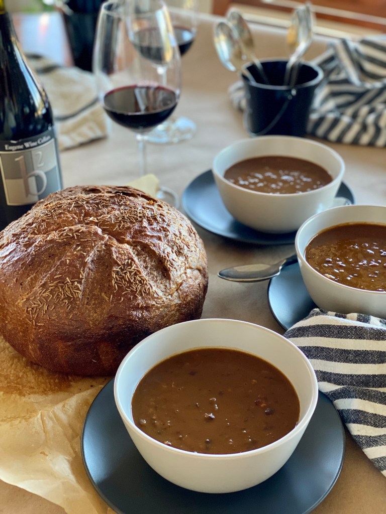 Bowls of Pumpkin Black Bean Soup, a loaf of bread, and wine on a table ready for a party.