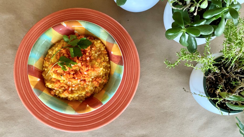 bowl of orange carrot risotto and spring plants
