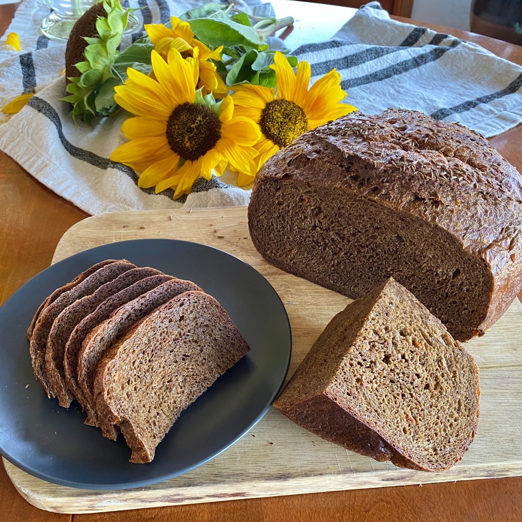 A loaf of caraway rye back bread on a cutting board with sliced and a wedge cut from it.