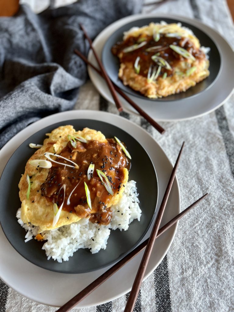 two plates of egg foo young with brown sauce on plates, with chopsticks.