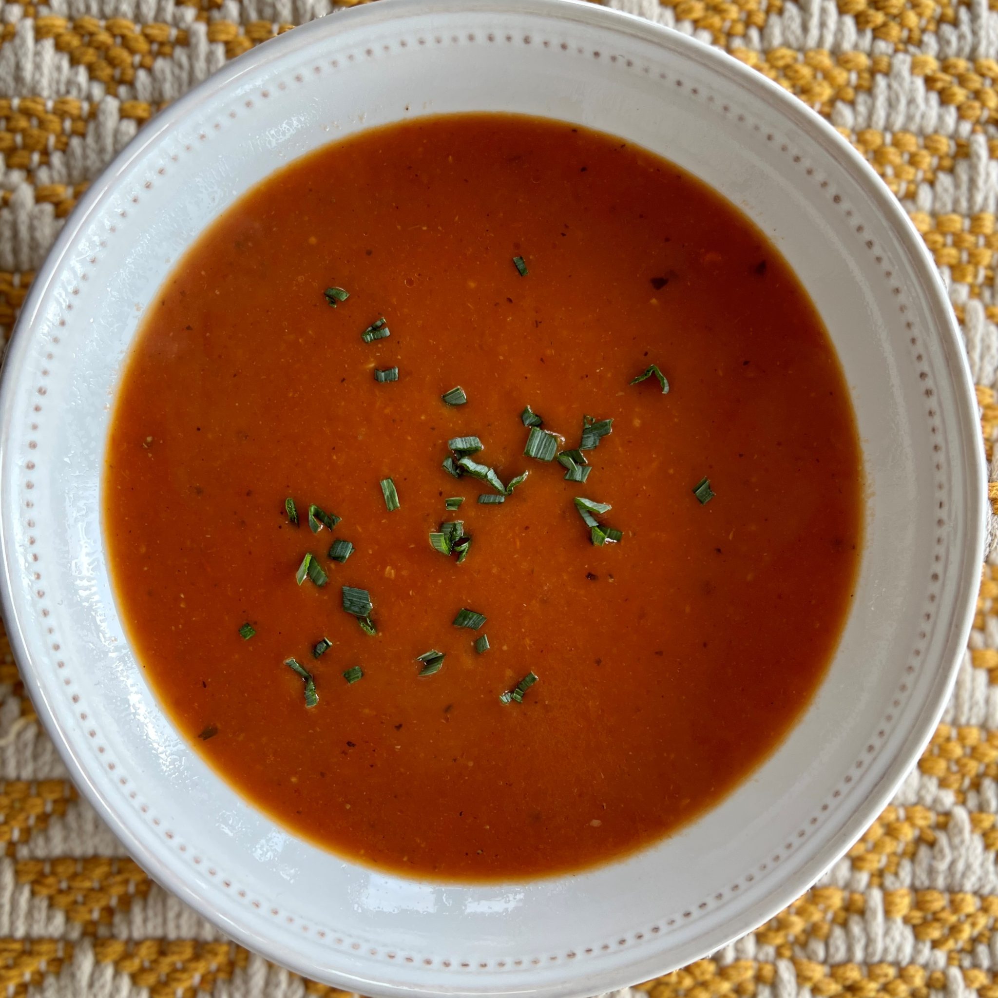 a top-down photo of a bowl of red tomato soup in a white bowl.