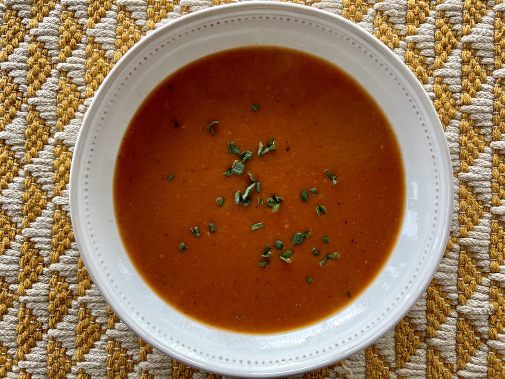 A top-down photo of a bowl of red tomato soup in a white bowl.