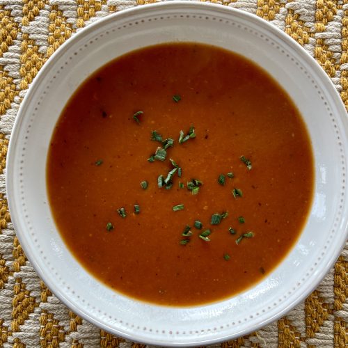 A top-down photo of a bowl of red tomato soup in a white bowl.