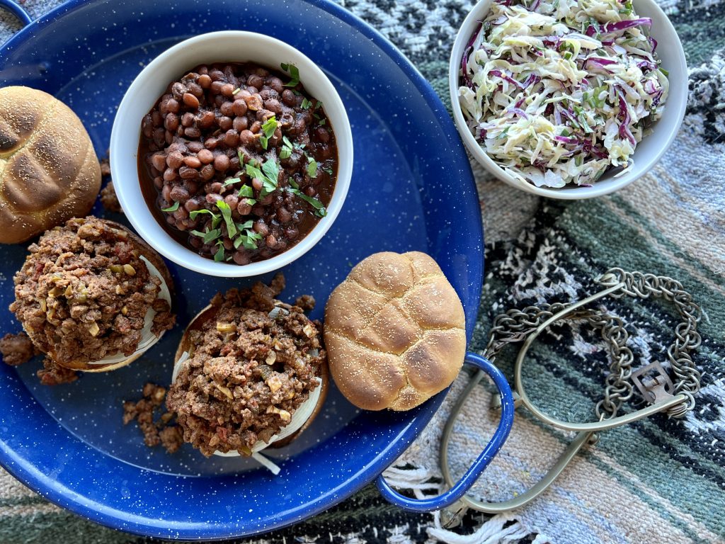 Cowboy sloppy joes on a platter with beans, next to spurs.