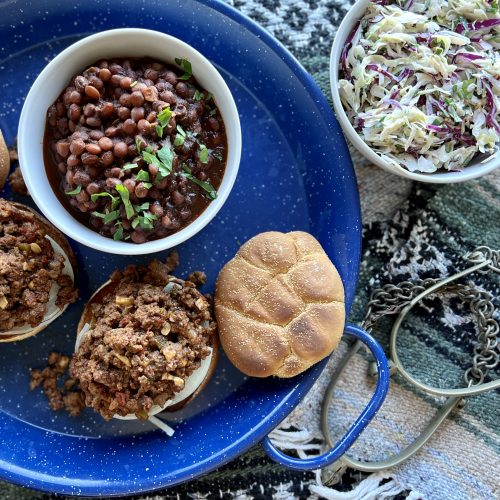 Cowboy sloppy joes on a platter with beans, next to spurs.