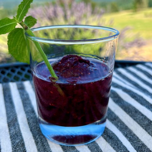 A blackberry summer cocktail on an outdoor table.