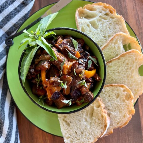 A bowl of caponata with slices of bread