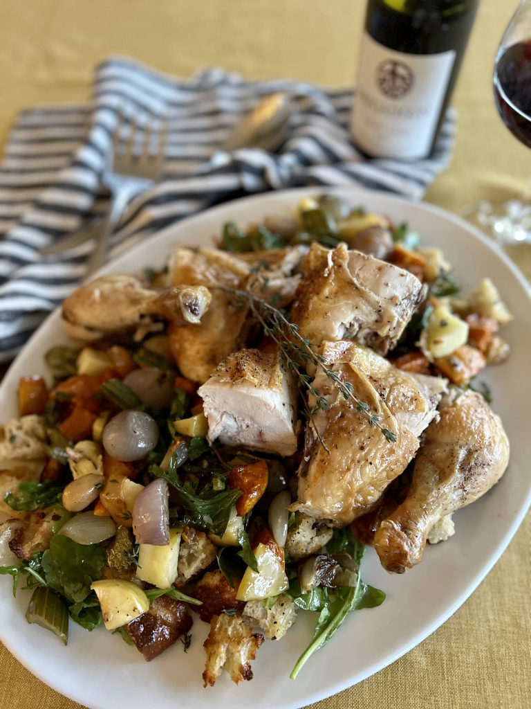a platter of rosted chicken and autumn bread salad with a bottle of wine.