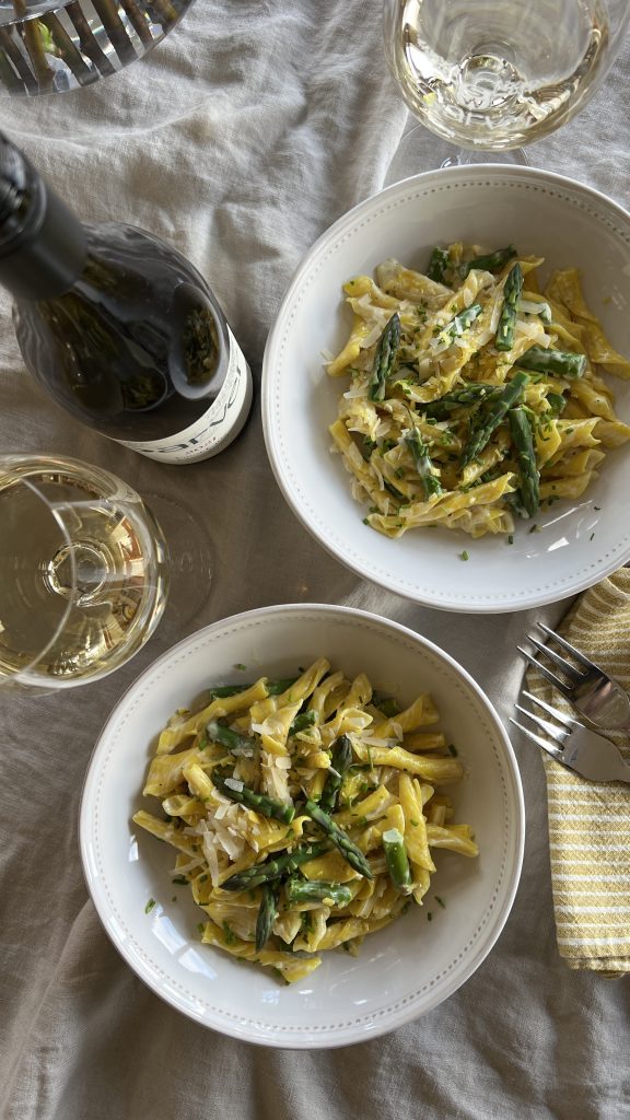 bowls of creamy lemon pasta on a table with wine bottle and glasses.